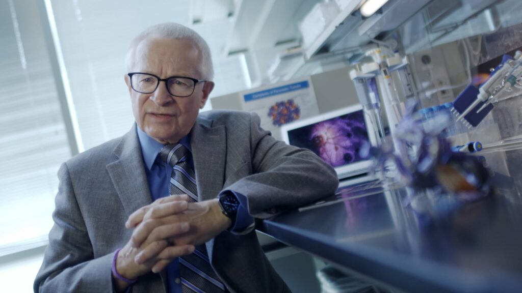 Man with glasses in suit sits in front of a lab station