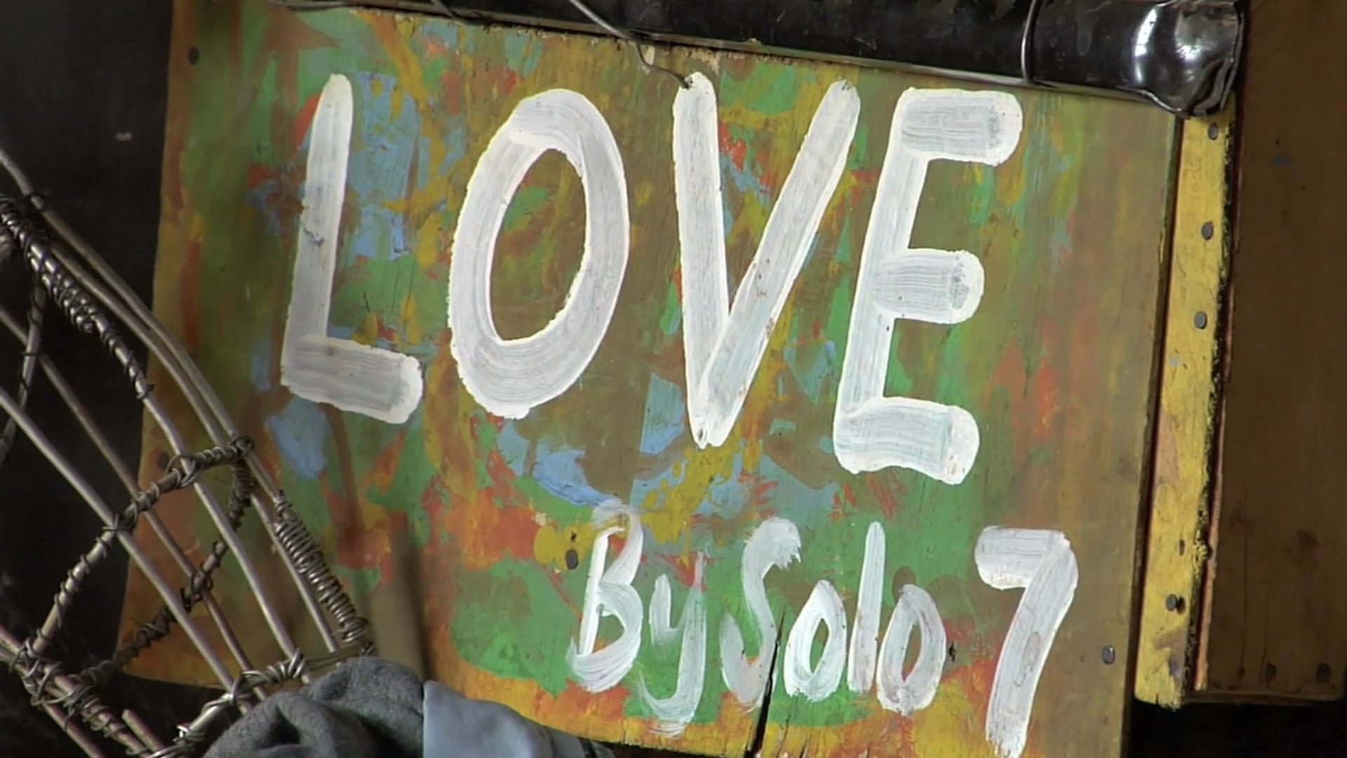 A poster saying LOVE by Solo7 with colorful paint behind it.